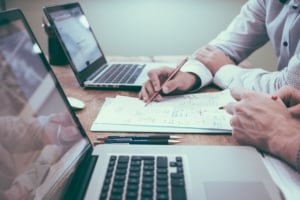 Person holding a pencil while reviewing reports and laptops 
